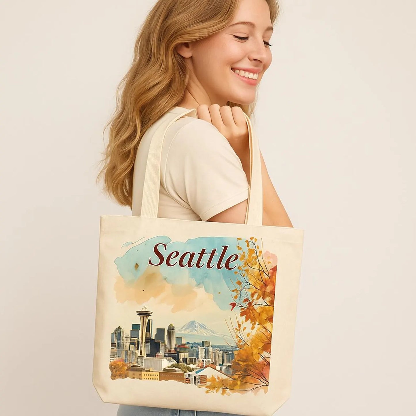 Smiling woman holding a beige tote bag with a watercolor Seattle print, neutral soft background.