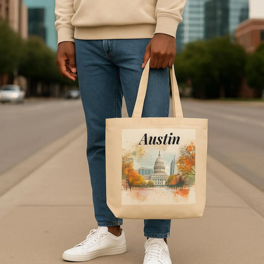 Close-up of man in jeans and white sneakers holding the Austin tote bag by the handles while standing on a street, showing the full design with Capitol art and autumn trees.