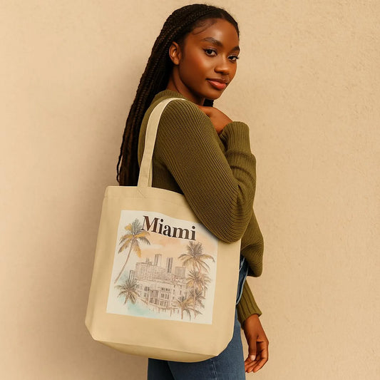 A stylish woman in a light olive outfit carries a Miami-themed organic cotton tote bag over her shoulder. The bag features a watercolor-style illustration of palm trees and city buildings. Neutral background highlights the eco-friendly lifestyle aesthetic